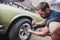 Young man removing wheels or tires from an old vintage car from the 60s or 70s in his home garage. Tools are seen around