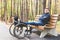 Young man resting sitting on a bench with his legs on his wheelchair.