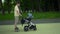 A young man rides a gyro scooter and carries a stroller. A modern father walks with a child in the park. Yellow T-shirt