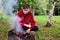 young man roasts meat, barbecue on coals on grill in nature. He\\\'s outside. Barbecue is located on green grass.