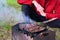 young man roasts meat, cooks barbecue on coals on grill in nature. Barbecue is located on green grass.