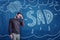 Young man with `SAD` chalk sign and pouring rain clouds drawn on blue board background