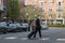 Young man with several a rolling suitcase and several shoulder bags crossing a street at a marked crosswalk in a small town with