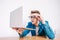 Young man in shirt and glasses he looks at the laptop in amazement and with a funny face sitting at the table on a white