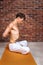 Young man showing breathing practices of belly, abdominal vacuum exercise. Yoga concept with copy space on brown brick wall
