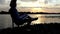 Young Man Sit in a Chair, Writes, And Smiles, on a Riverbank at Sunset