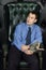 Young man sits with book looks away in leather armchair