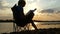 Young Man Sits on a Folding Chair on The Riverbank, Writes at Sunset in Slo-Mo