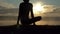 Young man sits on a lake bank and practices yoga at sunset in slow motion