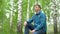 A young man sits in nature with headphones in his ears. A man sits on a stump in a birch forest and listens to music.