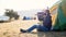 Young man sits on near the tent at campsite and drinking tea from thermos bottle