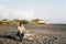 Young man sits on a snag on a sandy beach and looks at the sea