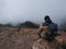 Young man sitting alone on a rock on Etna volcano, Sicily, Italy