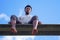 Young man sitting barefoot low angle view blue sky