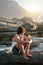 young man sitting on beach looking at sunset watching ocean contemplating journey