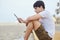 Young man sitting on beach reading ebook