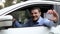 Young man sitting in the car and showing his new driver license with thumb up sign