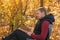 Young man is sitting on chair in the autumn forest and reading book. Mental recreation in nature. Quiet country life