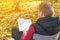 Young man is sitting on chair in the autumn forest and reading book. Mental recreation in nature. Quiet country life