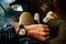 Young man sitting on chair wears a tartan shirt looking at his analog watch on his hand watching the time at the coffee shop.