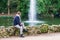 young man sitting contemplating a lake water fountain