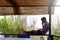 Young man sitting on the gazebo while looking at his smartphone. In the background the straws create a tropical scene