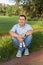 Young man sitting on grass in park and holds sneakers for newborn