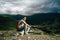 Young man sitting on hill. Dreamy male sitting on altitude and looking at Peaks of magnificent rocks located against