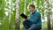 A young man is sitting in nature with a book in his hands. A man sits on a stump in a birch forest and reads a book.