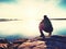 Young man sitting on a rock watching a gorgeous sunset on the sea. Hiker alone enjoy evening