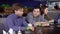 Young man sitting at the table in cafeteria eating sweet tasty dessert with whipped cream and talking with friend