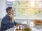 A young man is sitting and talking on a mobile phone and work with a laptop on the table in the living room. On the table, there