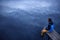 Young man sitting on a wooden dock, looking at skies reflecting