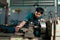 A young man in a small family-owned factory, is using a lathe, and carefully controls the lathe with his hands, with a serious