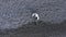 Young man with smartphone sitting on pebble beach at sea shore aerial view