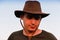 Young man smiling farmer in cowboy hat at field against blue sky. Portrait of millennial man standing on nature