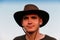 Young man smiling farmer in cowboy hat at field against blue sky. Portrait of millennial man standing on nature