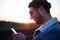 Young man smiling with smartphone in his hands on the background of sunset