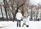 Young man with a son and baby in stroller walking in snowy park
