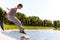 Young man in sportswear jumping and practicing parkour outside on stone fence over river embankment on clear summer day