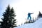 Young man in sportswear snowboarding over pine trees background