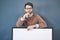 Young man standing behind an empty sign with copyspace. Smiling, attractive and smart male holding a blank board