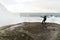 Young man standing on cliffs in front of the wild ocean with waves clashing against the rocks at Bunes Beach on Lofoten Islands in