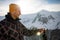 Young man standing on the edge of a mountain cliff, using an action camera to take a photo of snowy mountains.