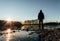 Young man standing on ice in pond with frozen shore, sun and trees