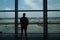 Young man is standing near window at the airport and watching plane before departure.