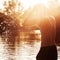 A young man is standing in a river and washing his face against the sunset.