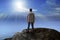 Young man standing on rock mountain and looking to the sun