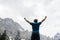 Young man standing victorious with his arms raised high surrounded with mountains