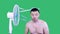 Young man stands by the cooling fan  isolated on green background.Chromakey. Close-up portrait.Flushed man feeling hot in front of